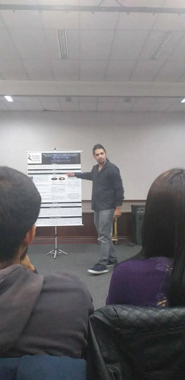 Lucas apresentando o banner da sua pesquisa de conclusão de curso para uma plateia